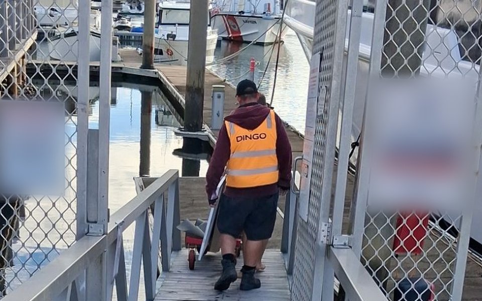Dingo crew member in a Dingo hi-vis vest wheeling a benchtop on a trolley down a marina gangway