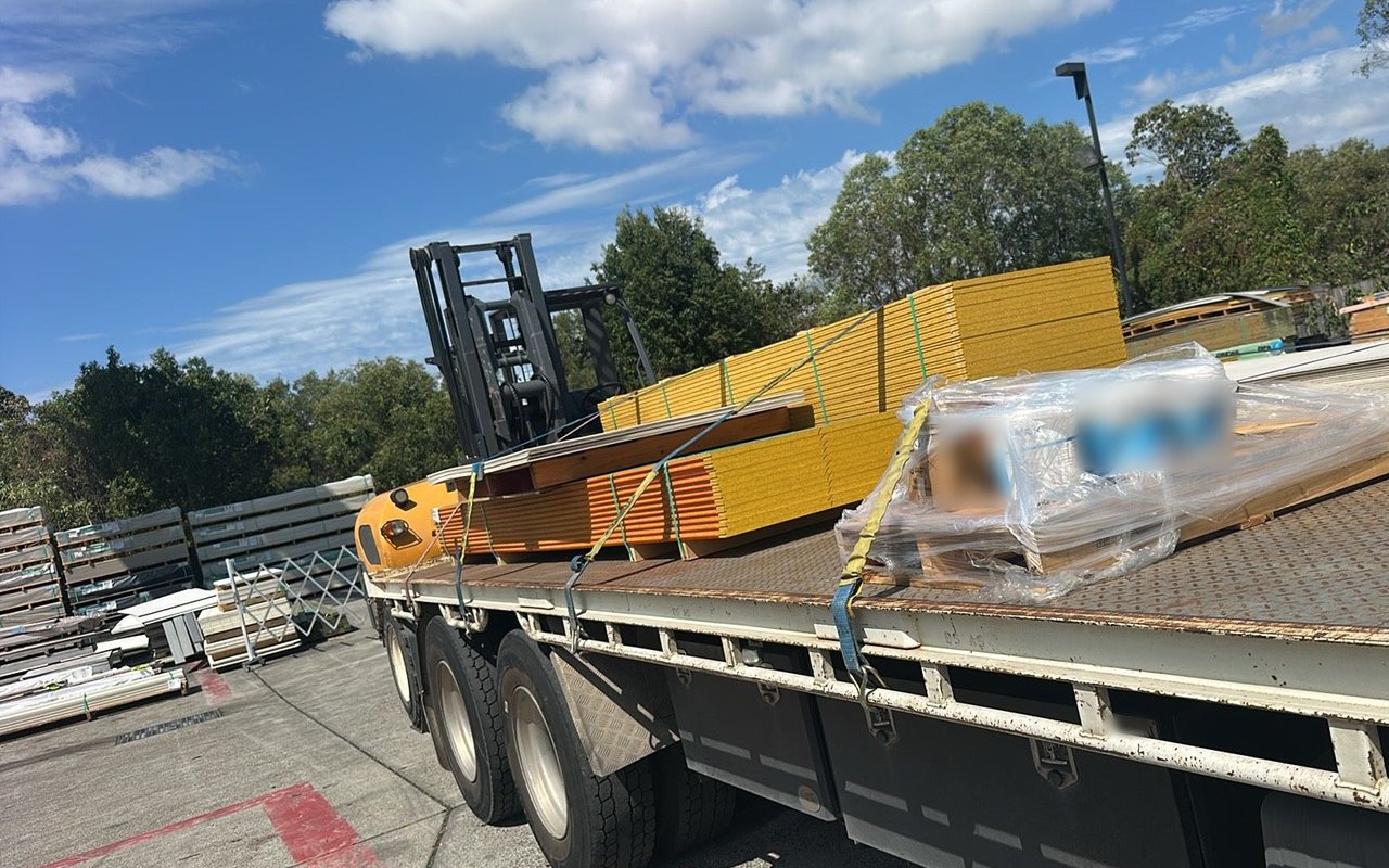 Tray truck loaded with strapped flooring sheets and a pallet, with the truck-mounted forklift carried on the back